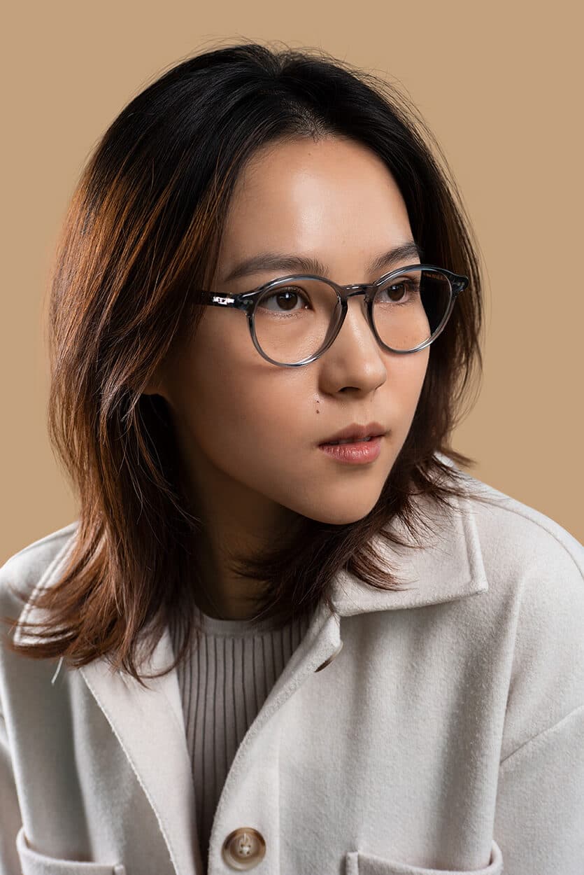 eine frau traegt eine dunkelblaue transparenter kunststoff korrektionsbrille und eine weisse jacke